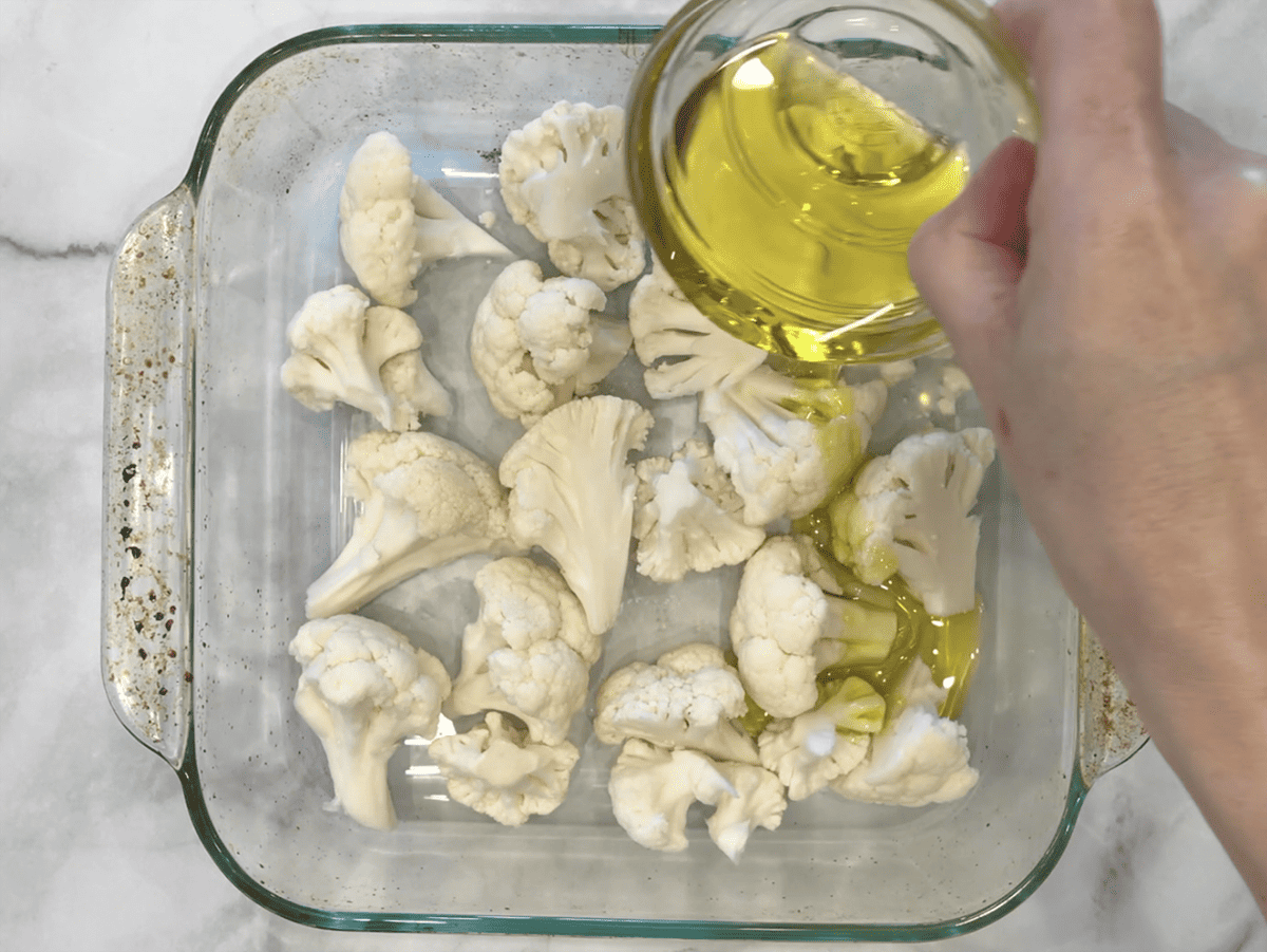 Adding olive oil to cauliflower florets in the pan.