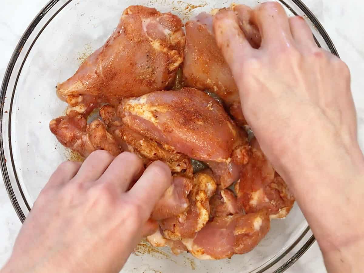 Using hands to mix spices into boneless chicken thighs.