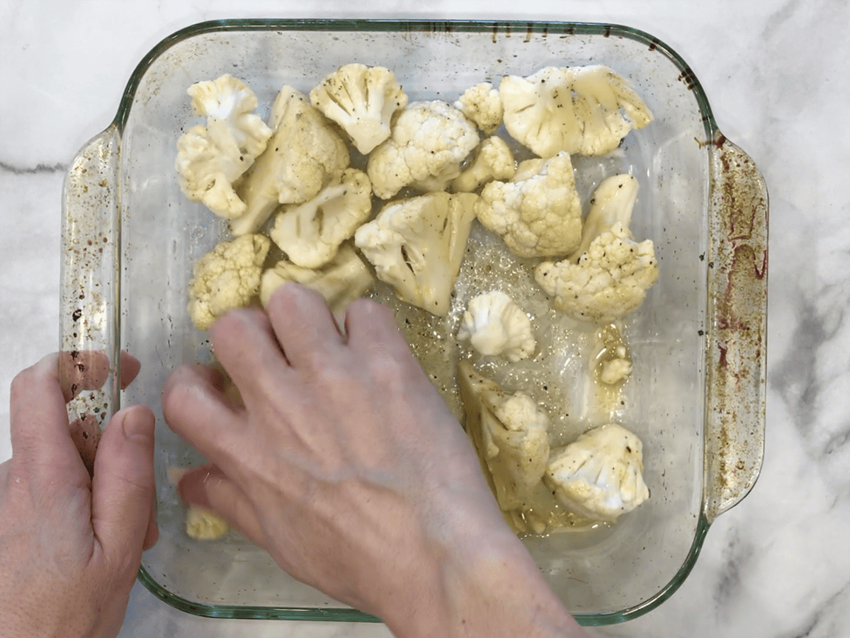Using hands to coat the cauliflower in olive oil and spices.