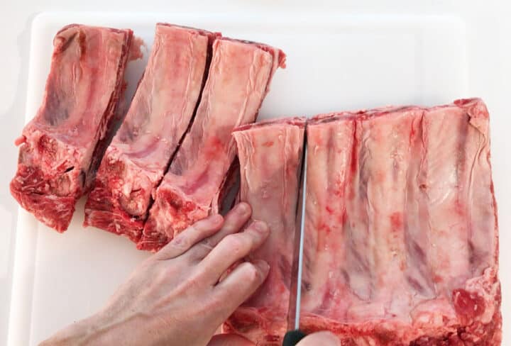 Cutting a rack of beef ribs into individual ribs.
