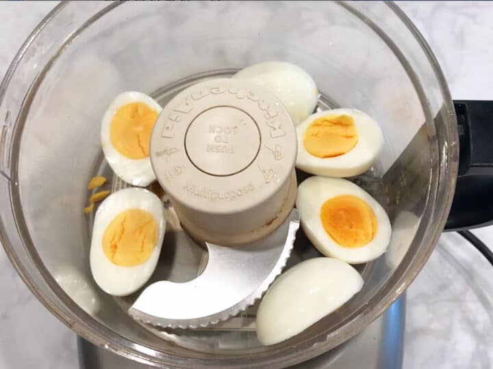 Hard-boiled eggs in a food processor bowl.