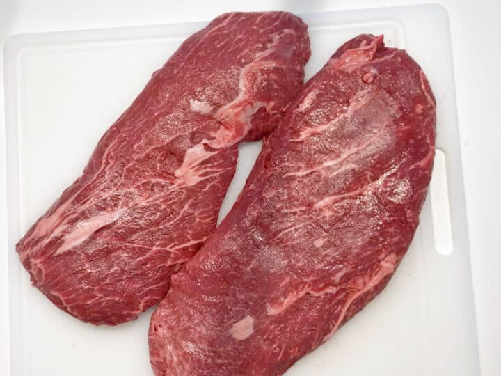 Two flat iron steaks on a cutting board.