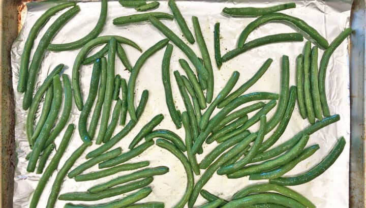 Green beans are spread evenly on a baking sheet.