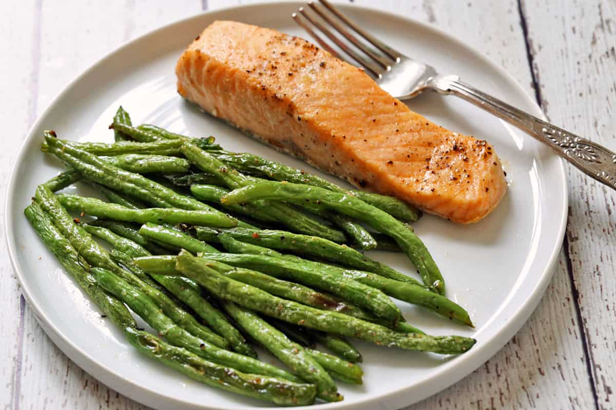 Baked salmon and roasted green beans on a white plate with  a fork. 