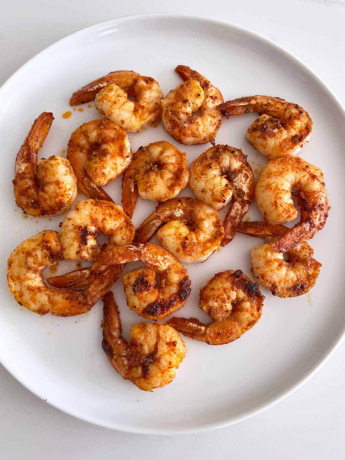 Heavily spiced grilled shrimp on a white plate.