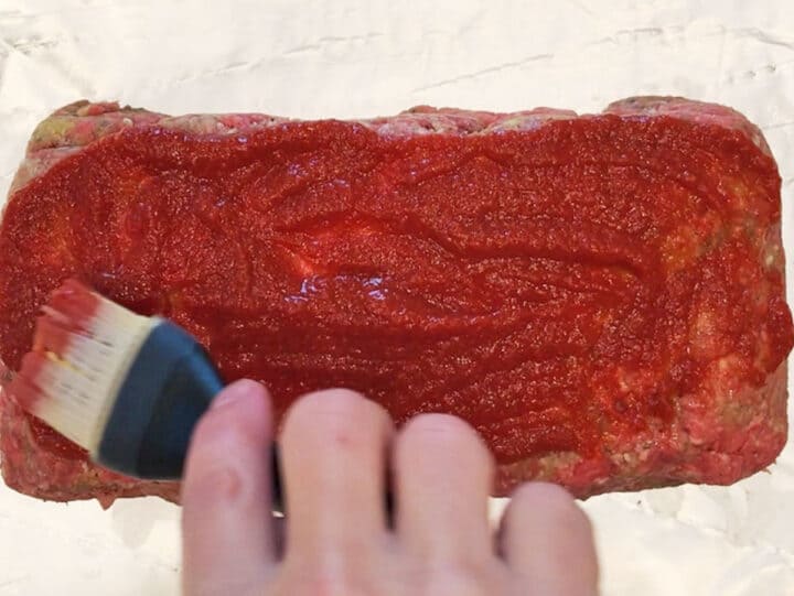Coating the meatloaf with ketchup.
