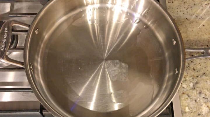 Heating oil in a stainless steel skillet.