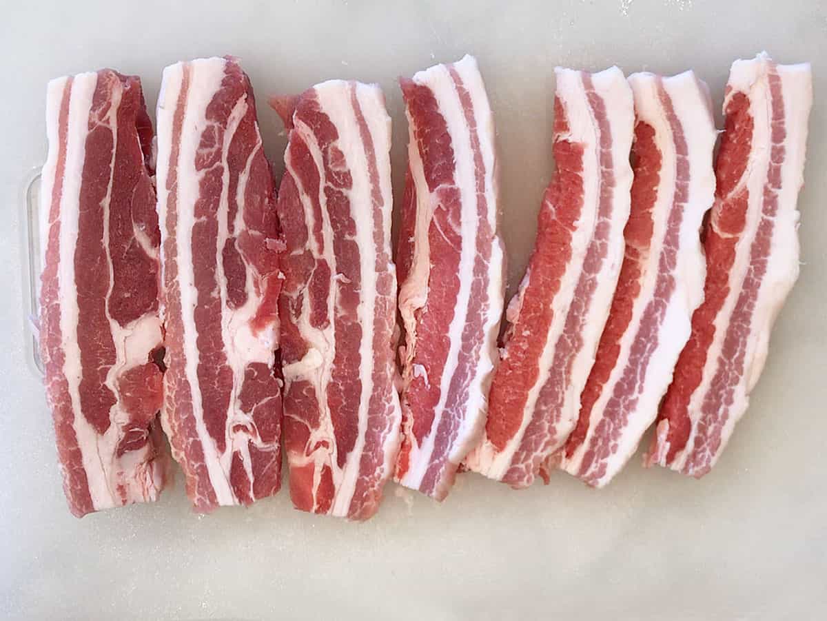 Pork belly slices on a cutting board.