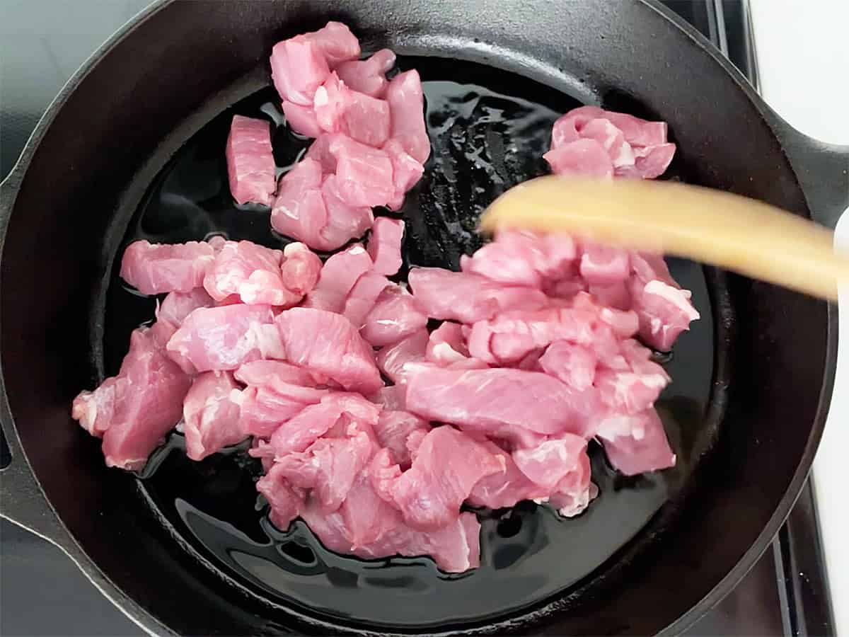 Stir-frying pork pieces in a skillet. 