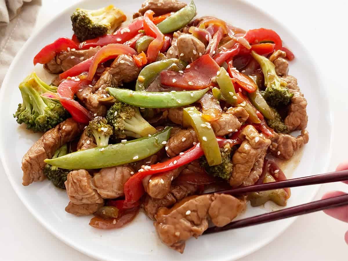 The stir-fry is served on a white plate with chopsticks. 