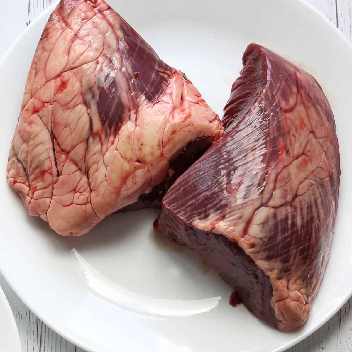 Two raw beef heart halves. One of them has a visible fat layer.
