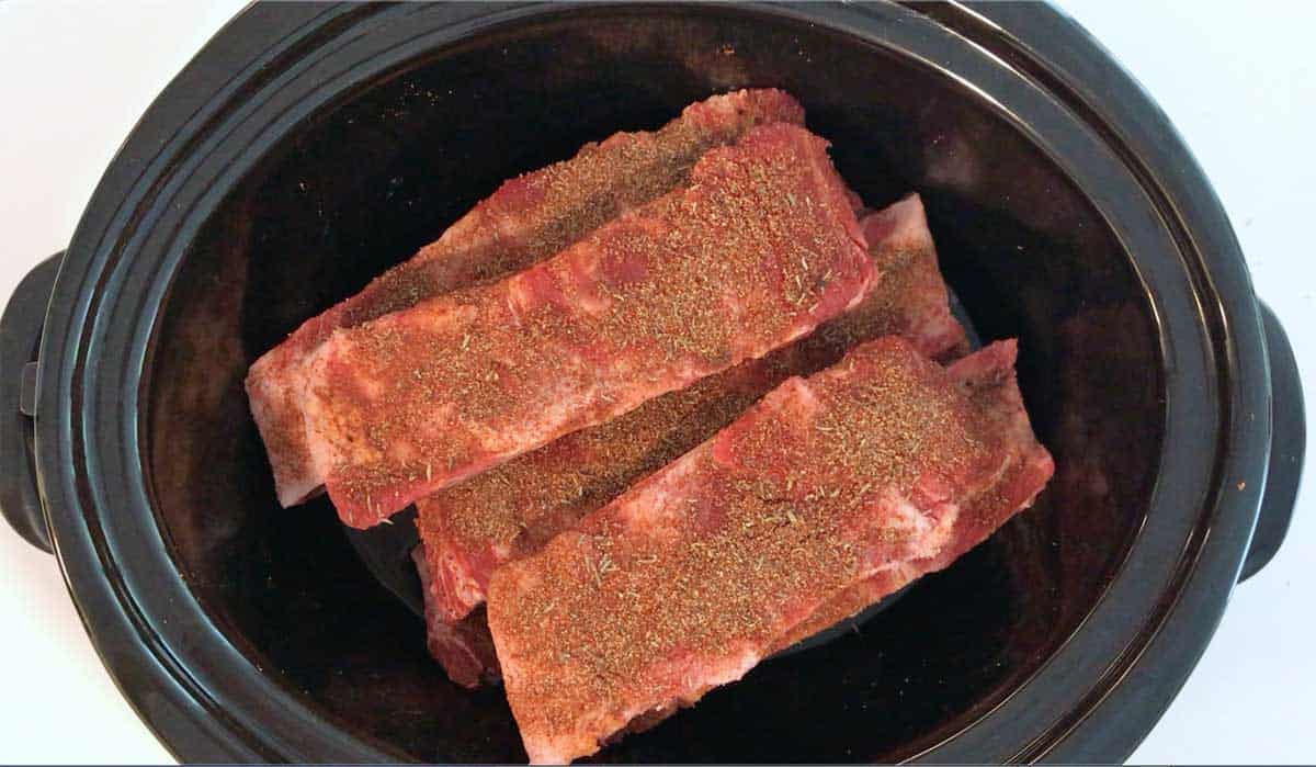 Beef ribs are layered in a slow cooker pan. 