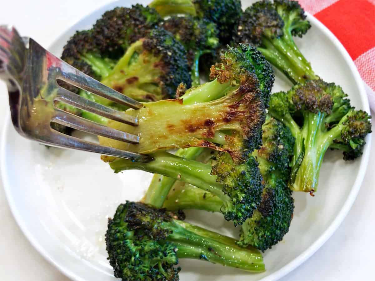 A fork holds up a roasted broccoli floret.
