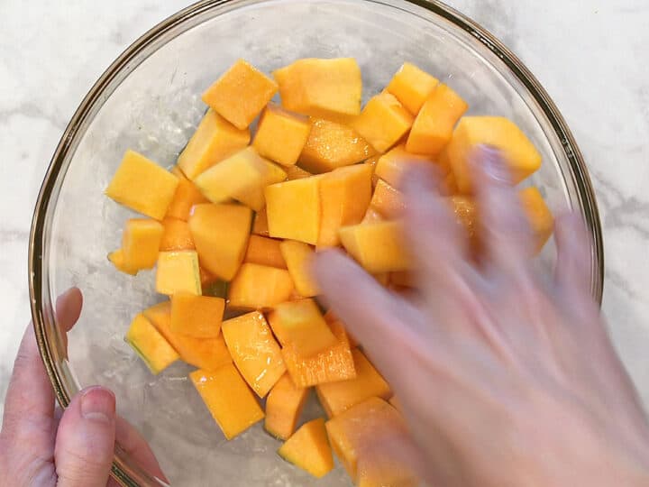 Using hands to mix the oil into the butternut squash cubes.