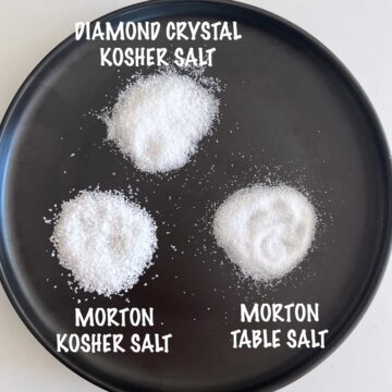 Three mounds of salt on a black plate: Diamond Crystal, Morton Kosher Salt, and Morton Table Salt.