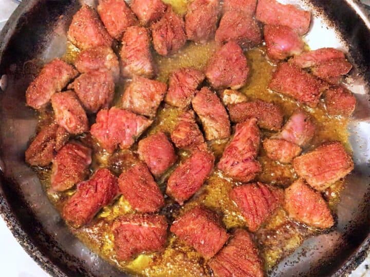 Cooking steak cubes in a skillet.