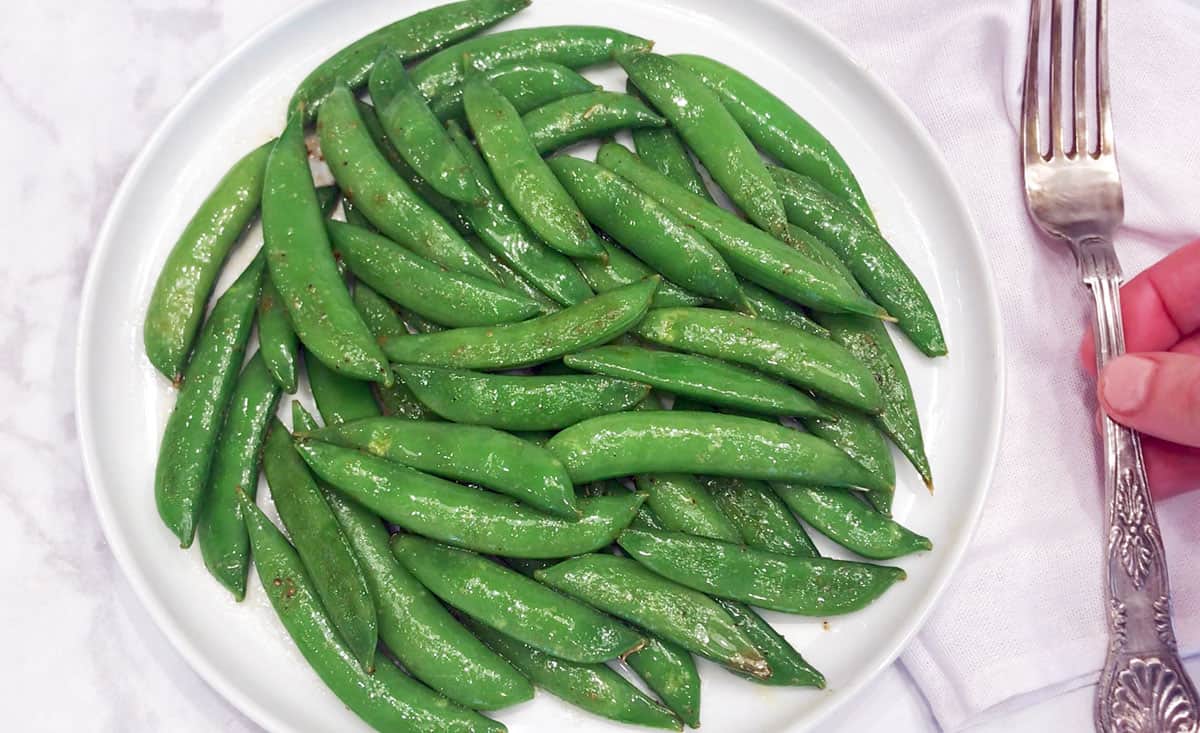 Sugar snap peas are served on a plate with a fork.