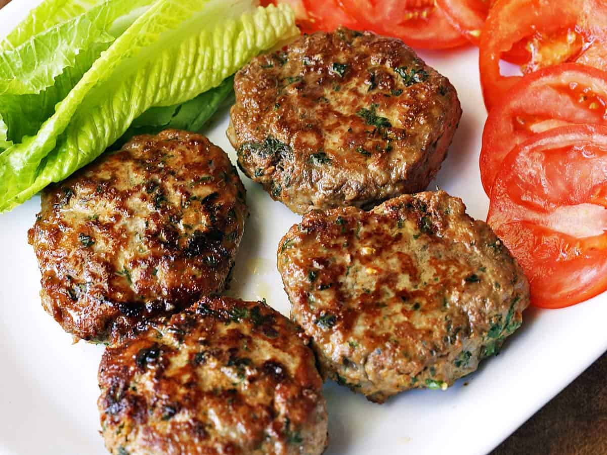 Turkey burgers on a plate with tomatoes and lettuce. 