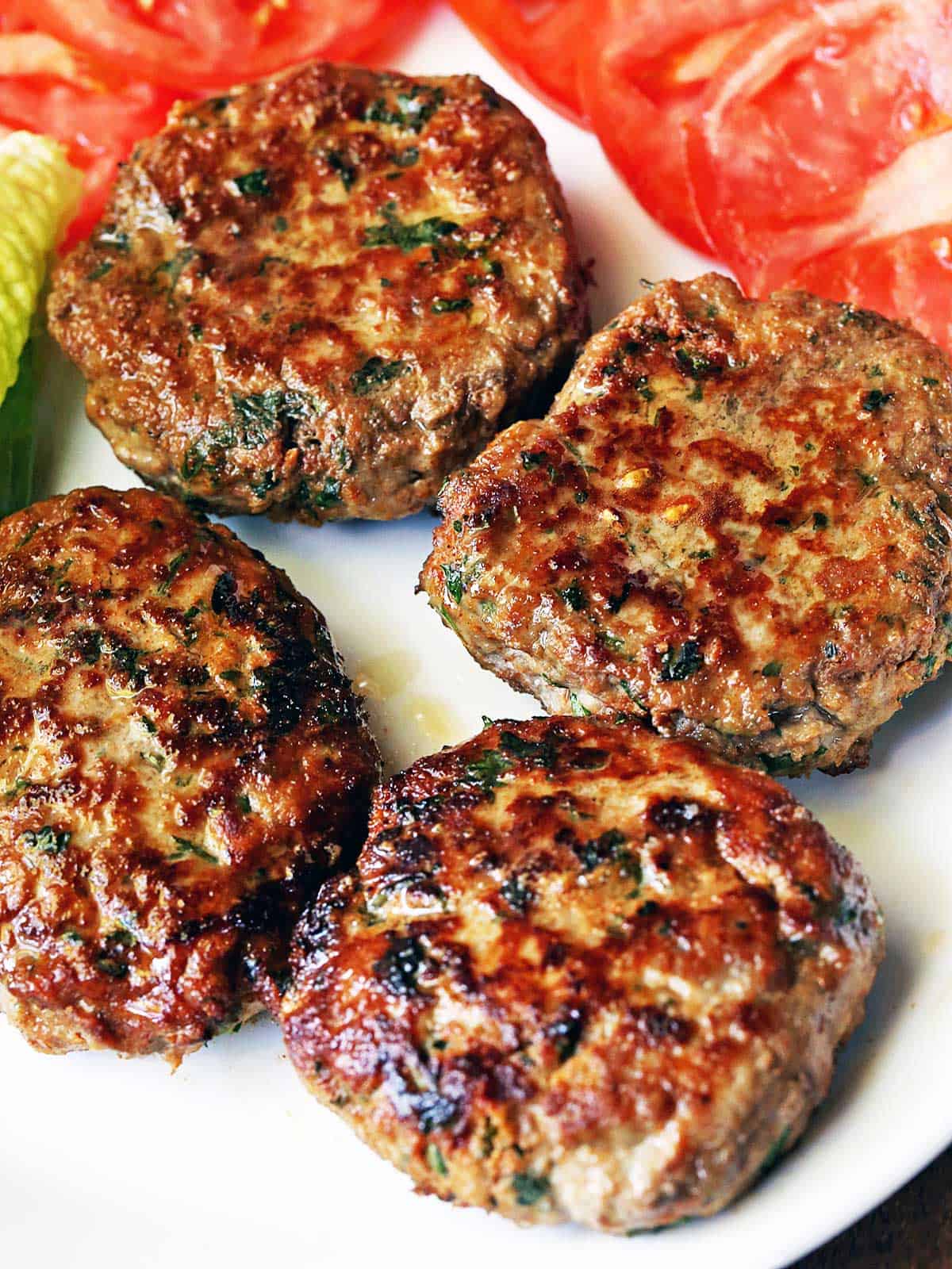 Four turkey burgers served with lettuce and tomatoes. 