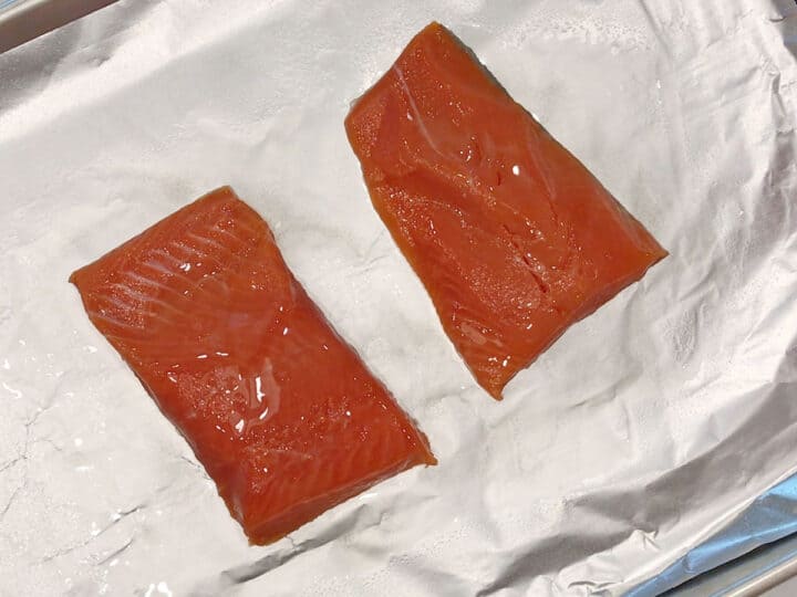 Two salmon fillets on a foil-lined baking sheet.