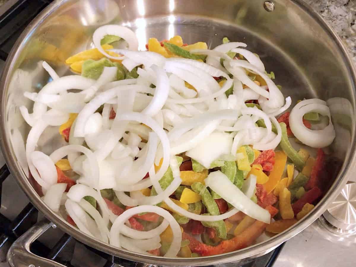 Sliced peppers and onions in a skillet.