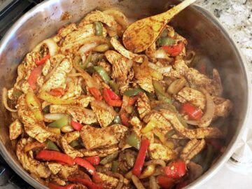 Cooking chicken, vegetables, and spices in a skillet.
