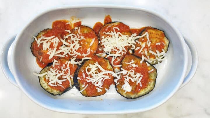Eggplant slices topped with marinara and mozzarella in a casserole dish.