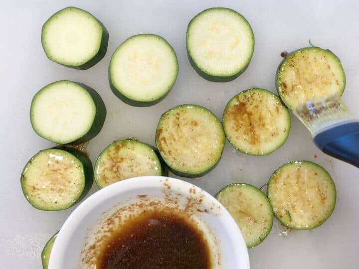 Brushing raw zucchini with an olive oil-balsamic marinade.