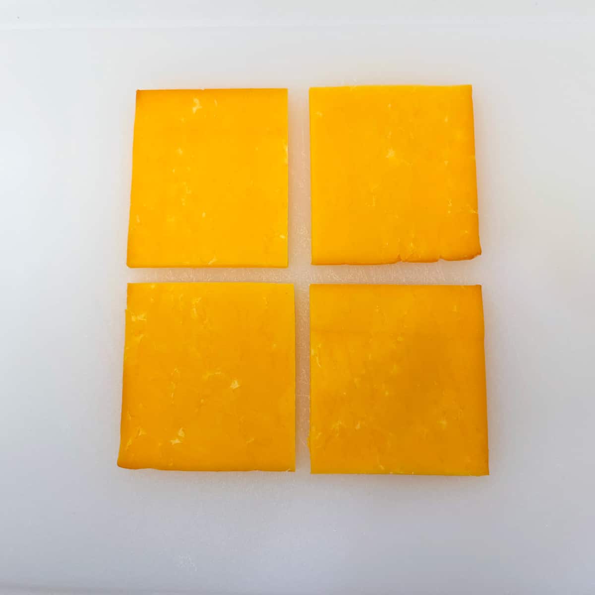 A slice of cheese on a cutting board, cut into four squares.