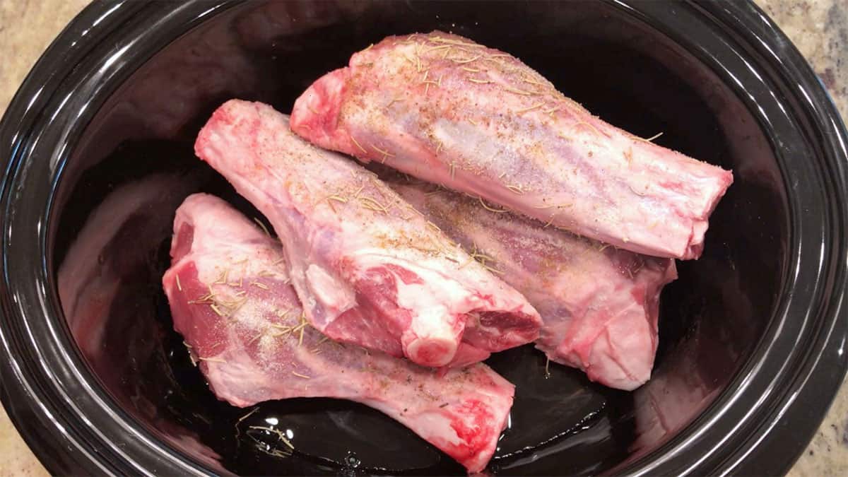 Lamb shanks in a slow cooker pan.