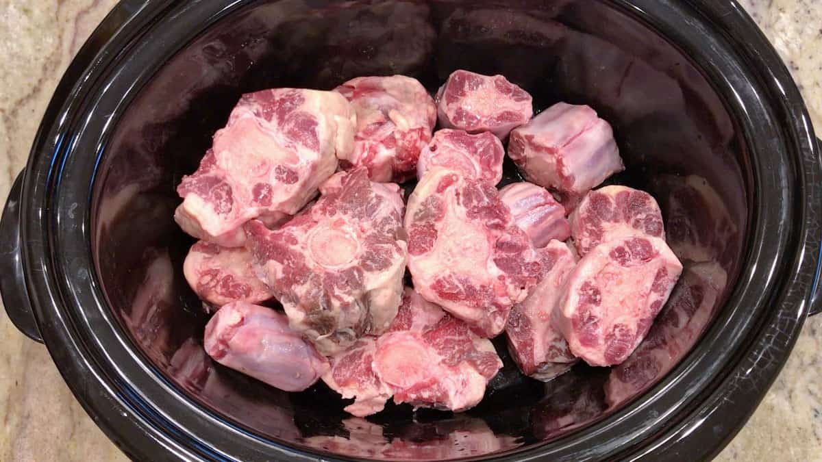 Raw oxtails in a slow cooker pan.