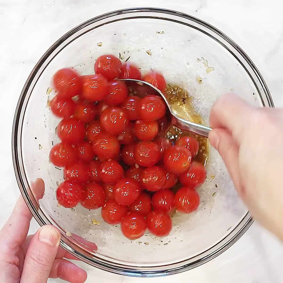Mixing cherry tomatoes and seasonings in a bowl.