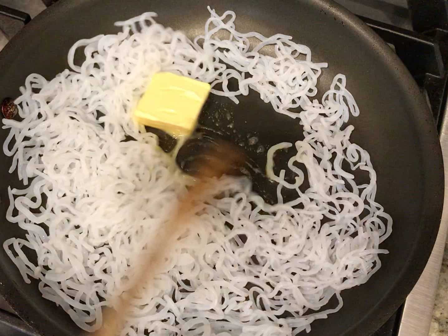 Adding butters to the noodles in the skillet.