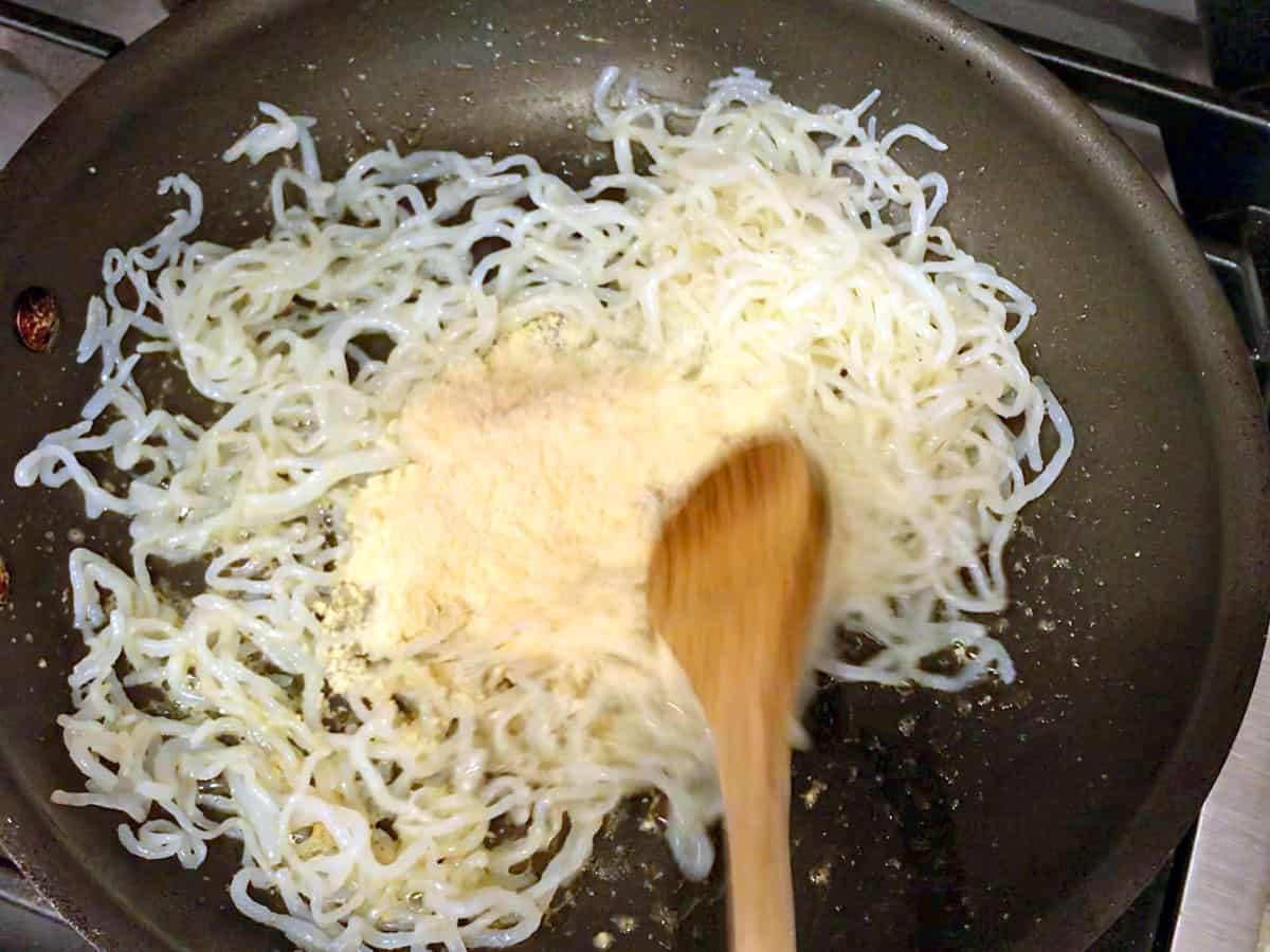 Adding parmesan to the noodles in the skillet.