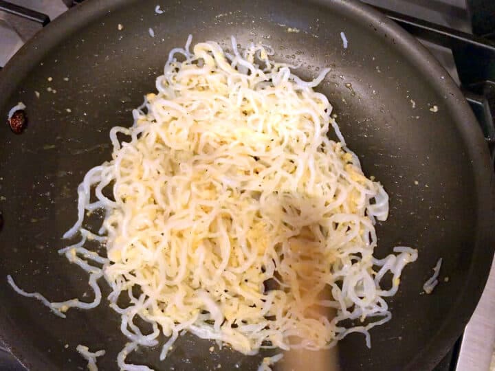 The noodles are coated in butter in the skillet.