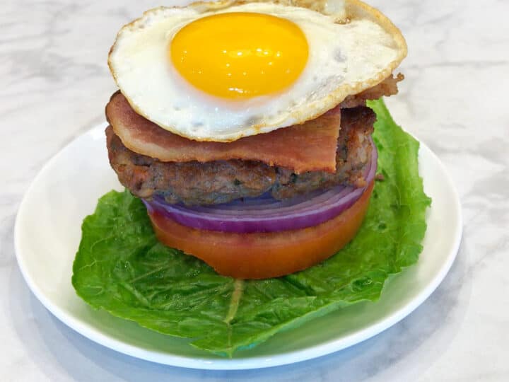 A bacon burger served on lettuce, tomato, and red onion, and topped with bacon and a fried egg.