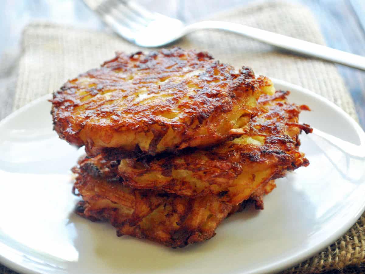 Three baked latkes stacked on a white plate.