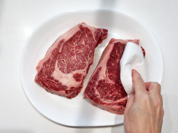 Blotting a ribeye steak with a paper towel.