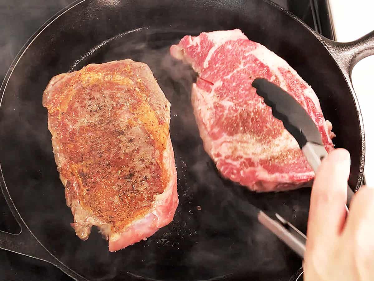 Flipping a ribeye steak with tongs.