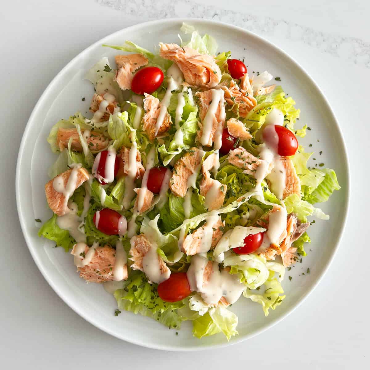 A salad made of lettuce, tomatoes, leftover salmon, and ranch dressing.