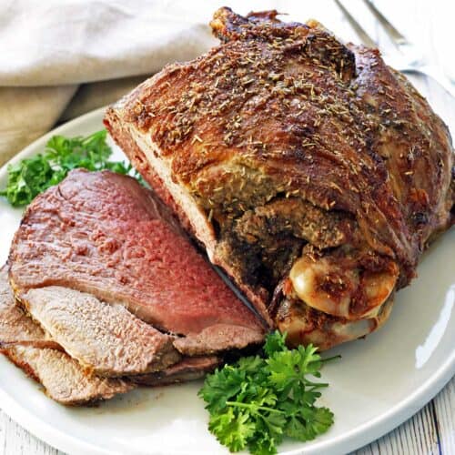A roasted leg of lamb, sliced, on a white plate.