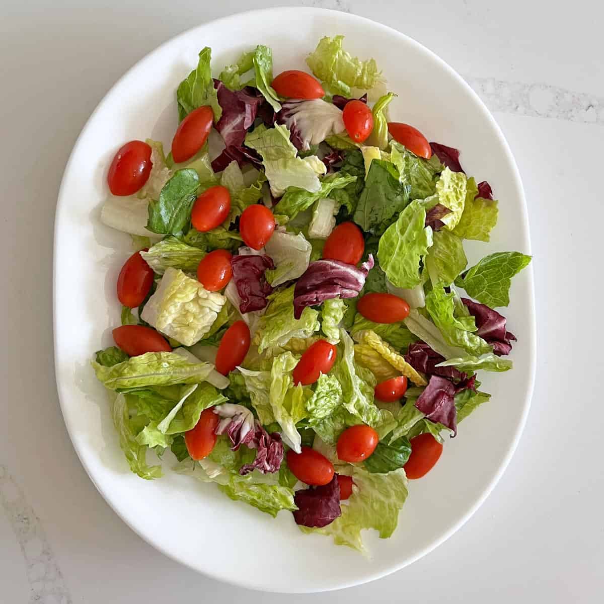 Mixed greens and cherry tomatoes on a white platter.