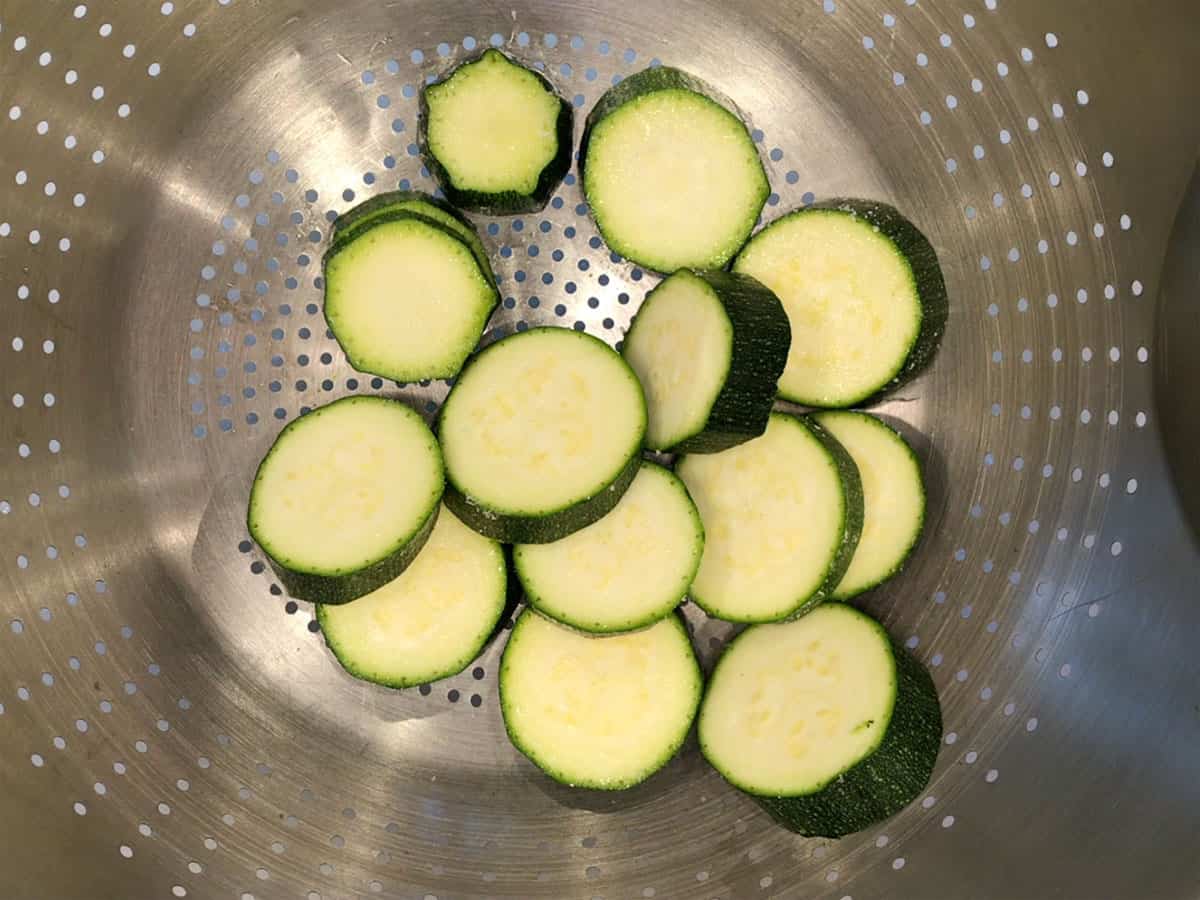 Zucchini slices draining in a colander.