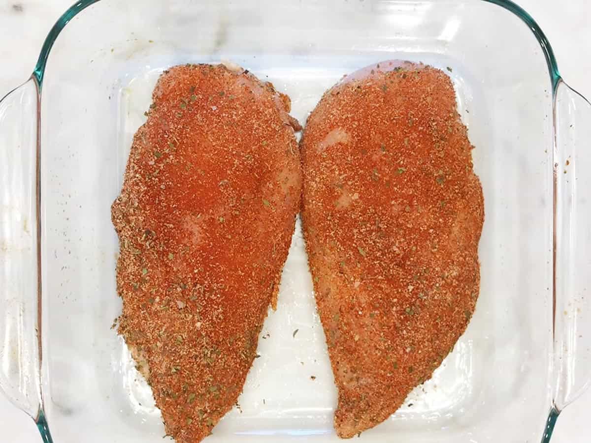 Two Cajun-spiced chicken breasts in a baking dish, before baking.