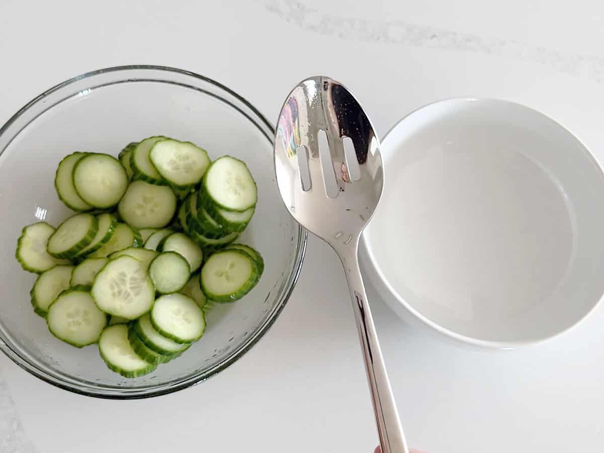 Using a slotted spoon to remove the cucumber slices from the marinade.