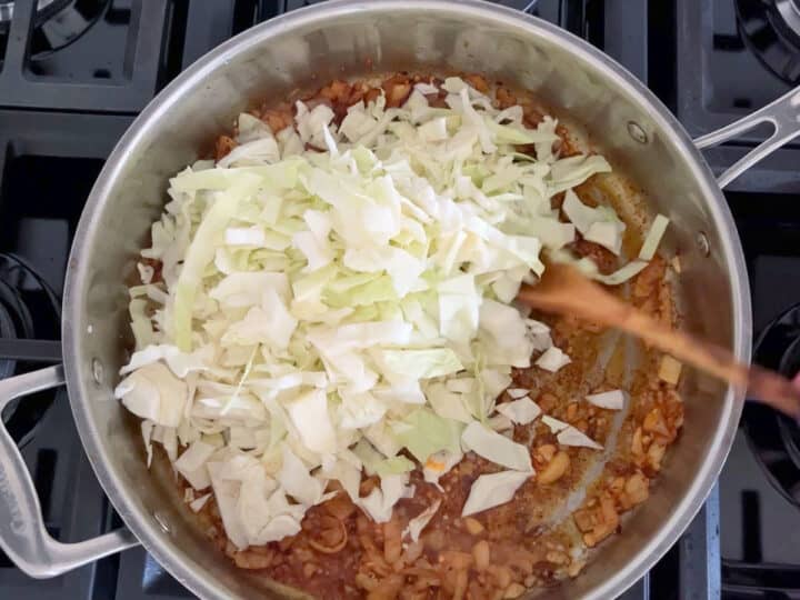 Adding chopped cabbage to the skillet.