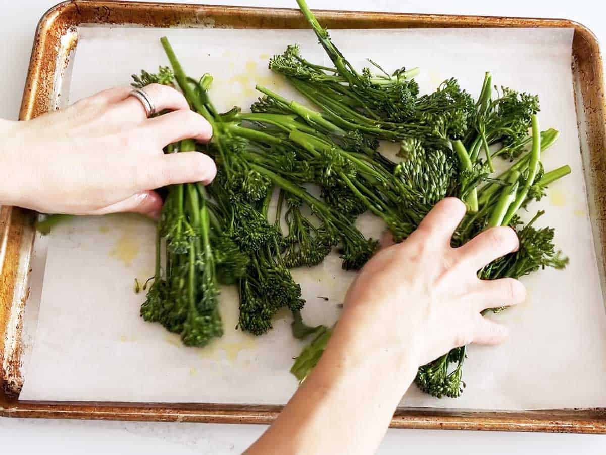 Coating the broccolini in the oil.