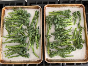 Raw broccolini on two parchment-lined, rimmed baking sheets.
