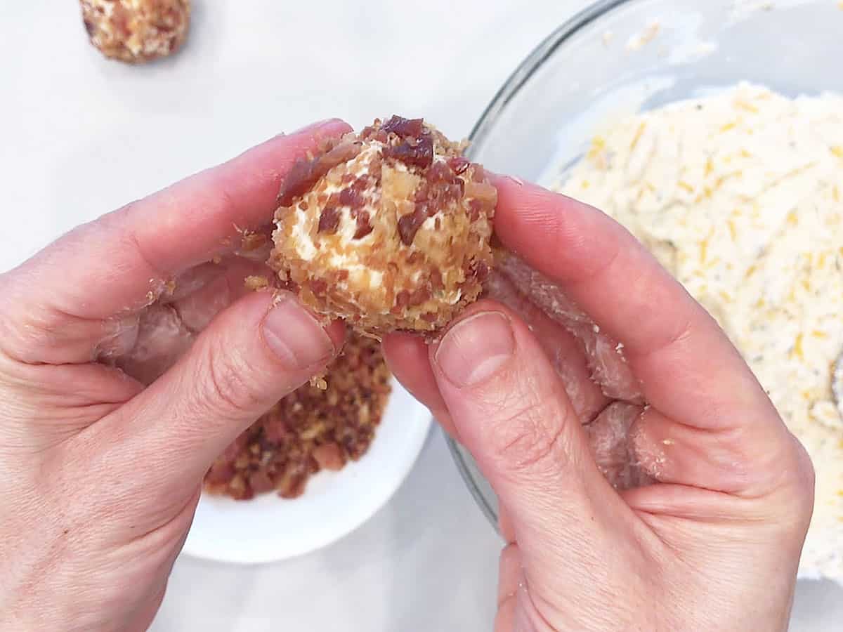 Two hands holding a bacon-covered cheese ball.