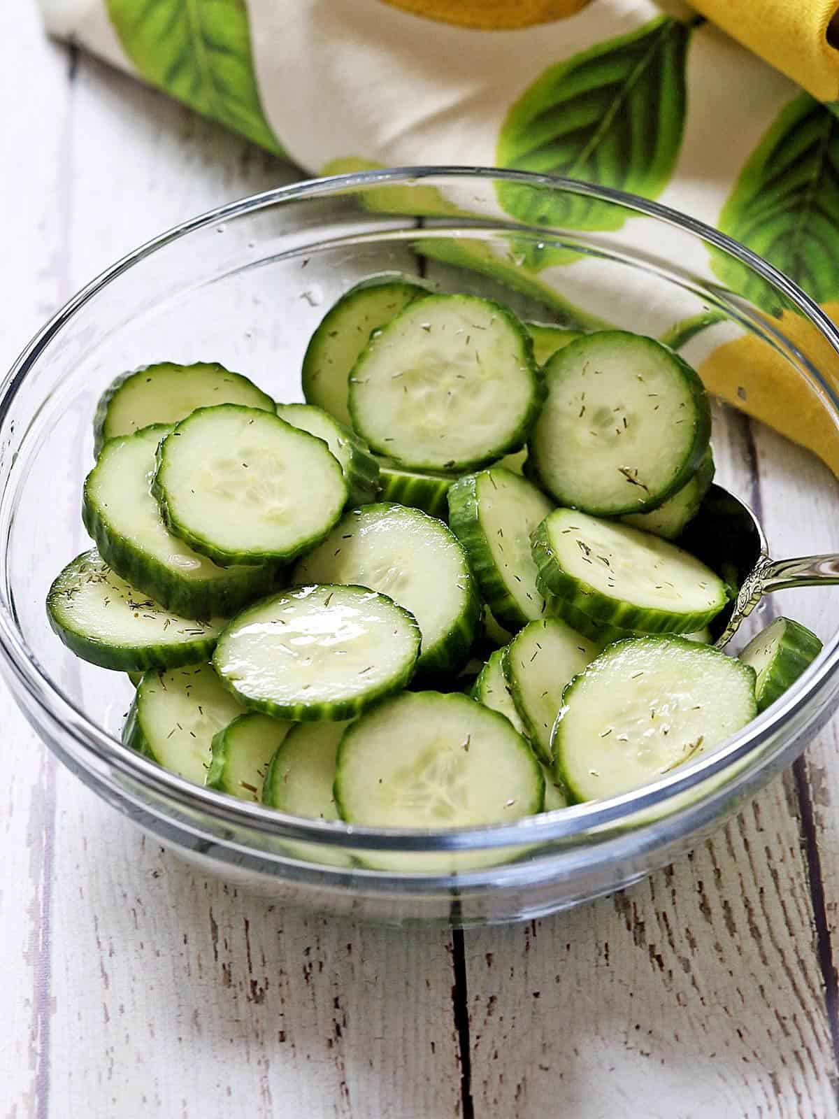 Cucumber vinegar salad is served in a bowl with a serving spoon.